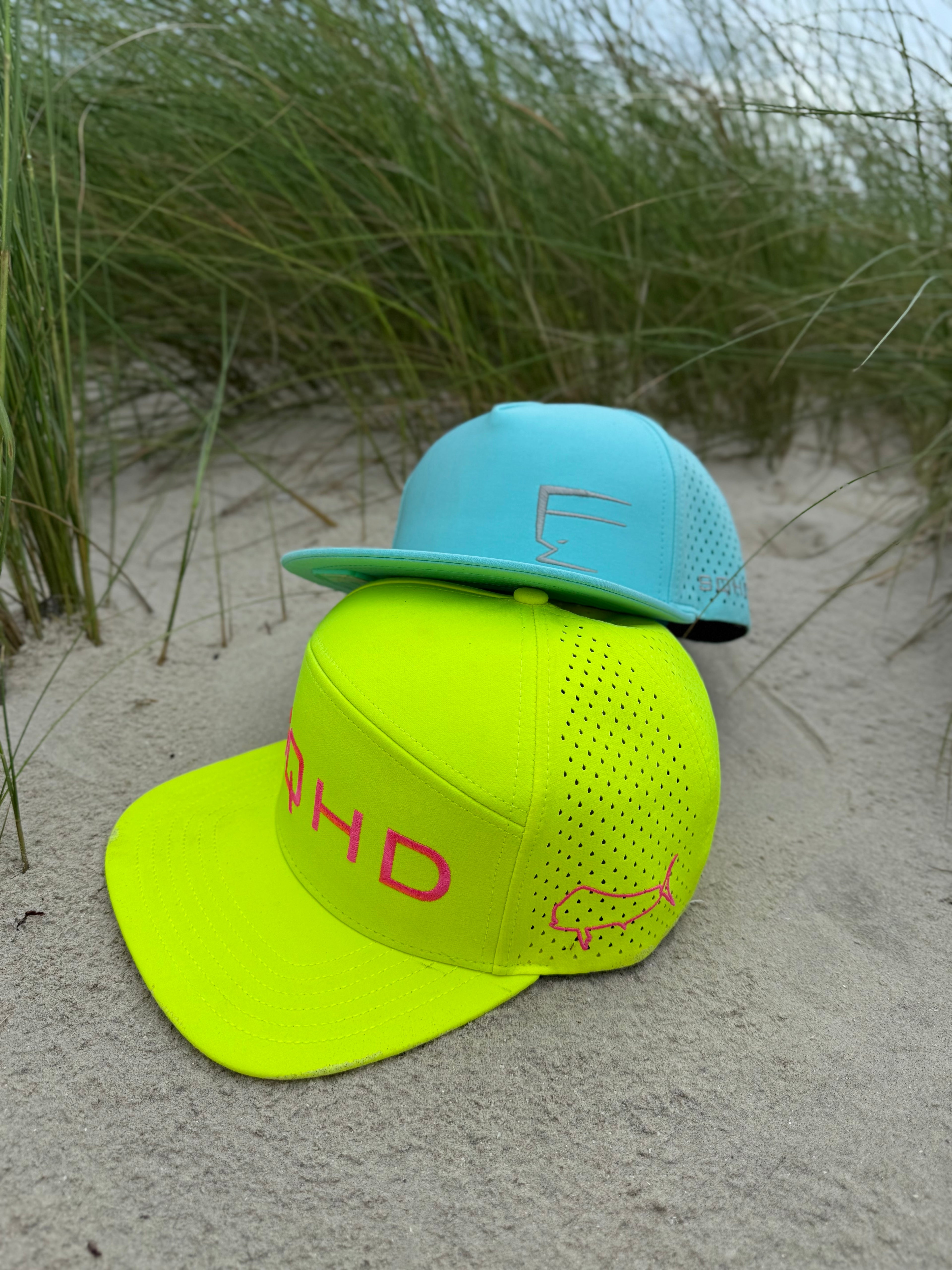 Two baseball caps, one yellow and one blue, on a sandy surface with grass in the background.
